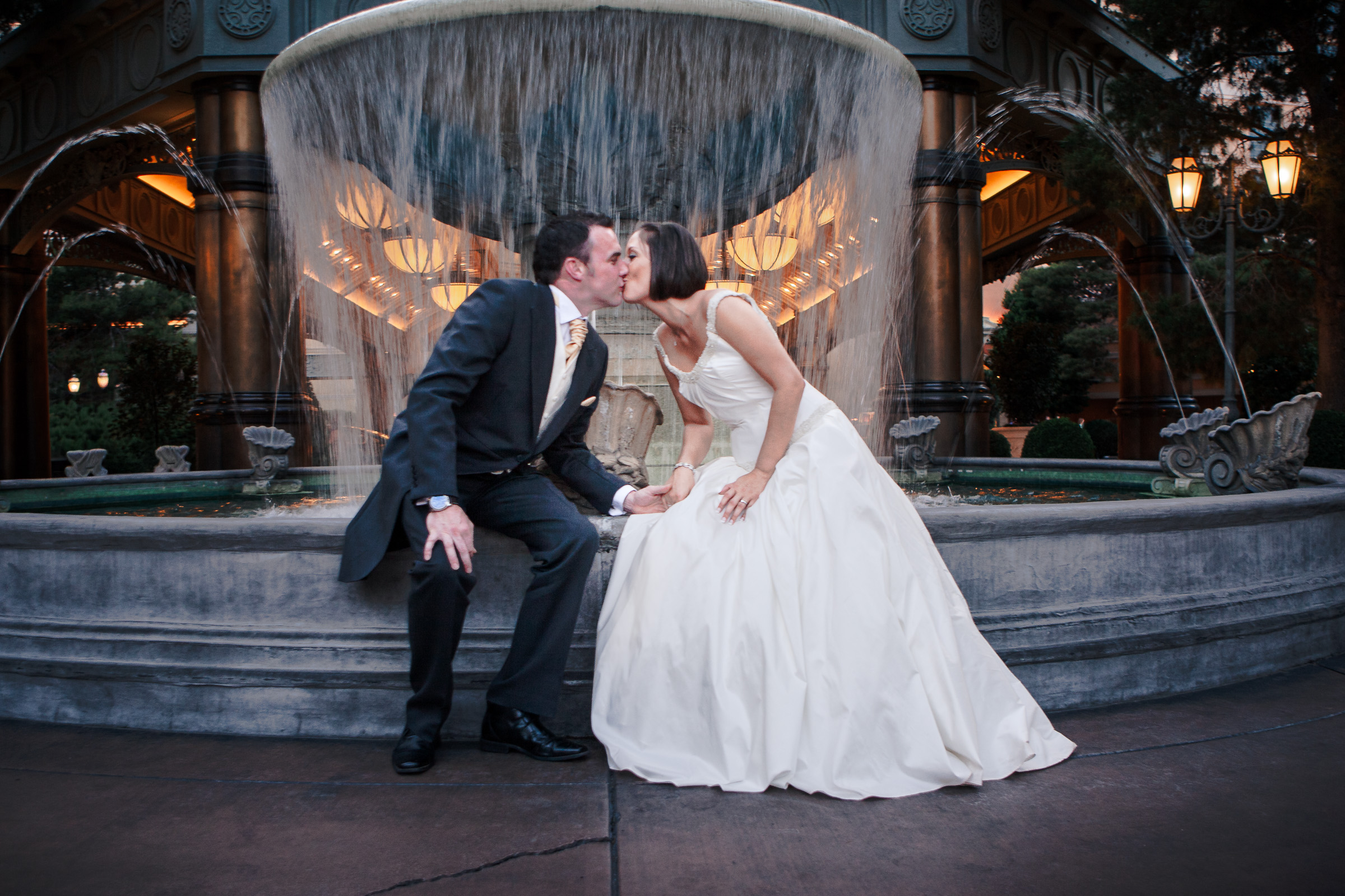 Destination Las Vegas wedding photographer capturing a couple kissing at a Bellagio resort fountain with cinematic evening lighting