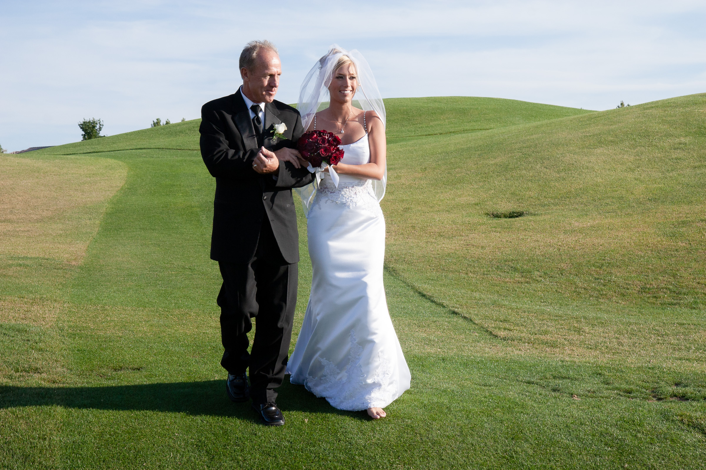 Father of the bride and bride walking through the golf course to the ceremony. Notice the bride is barefoot.