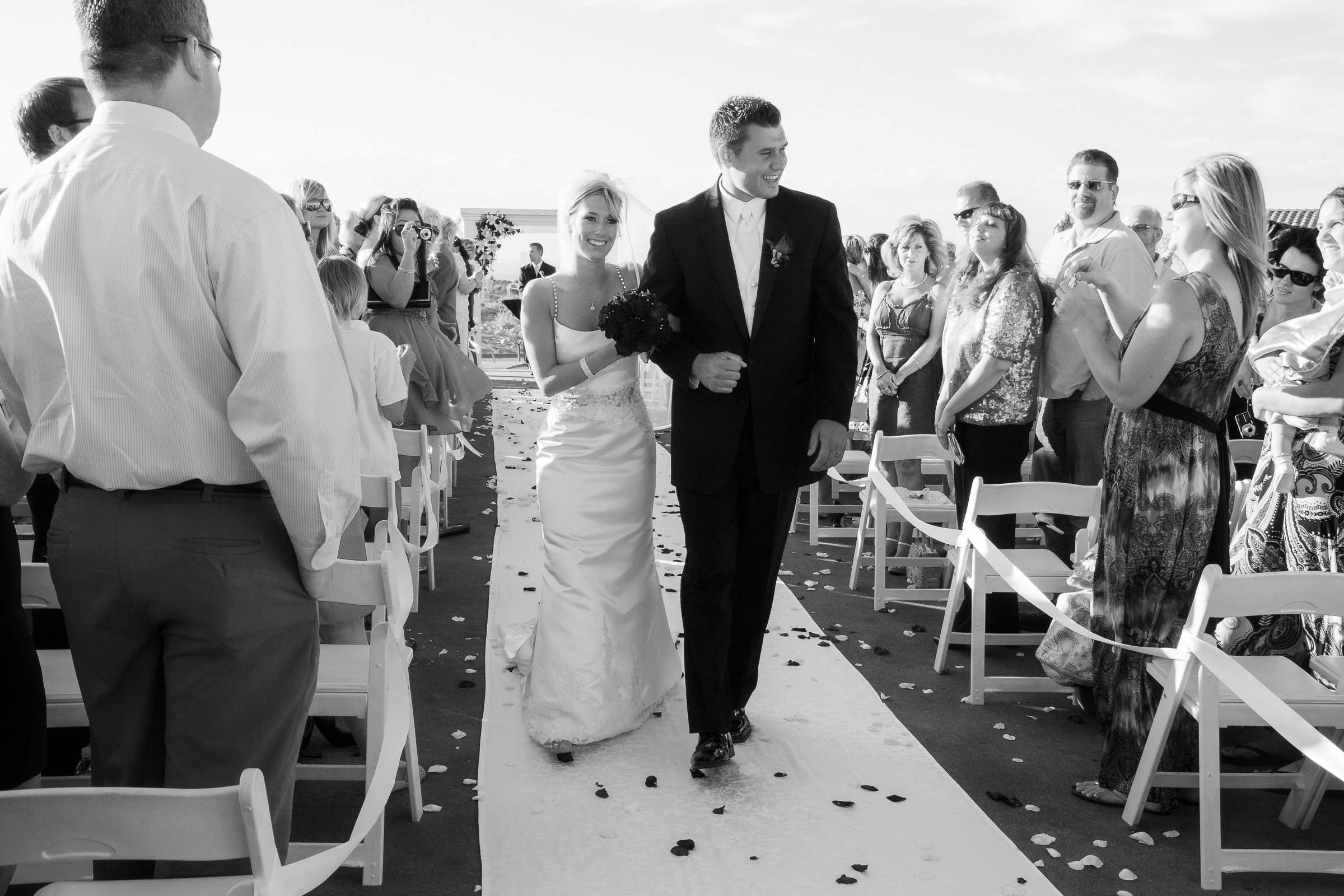 Black and white photo of bride and groom coming down the isle after the ceremony in bright sunlight