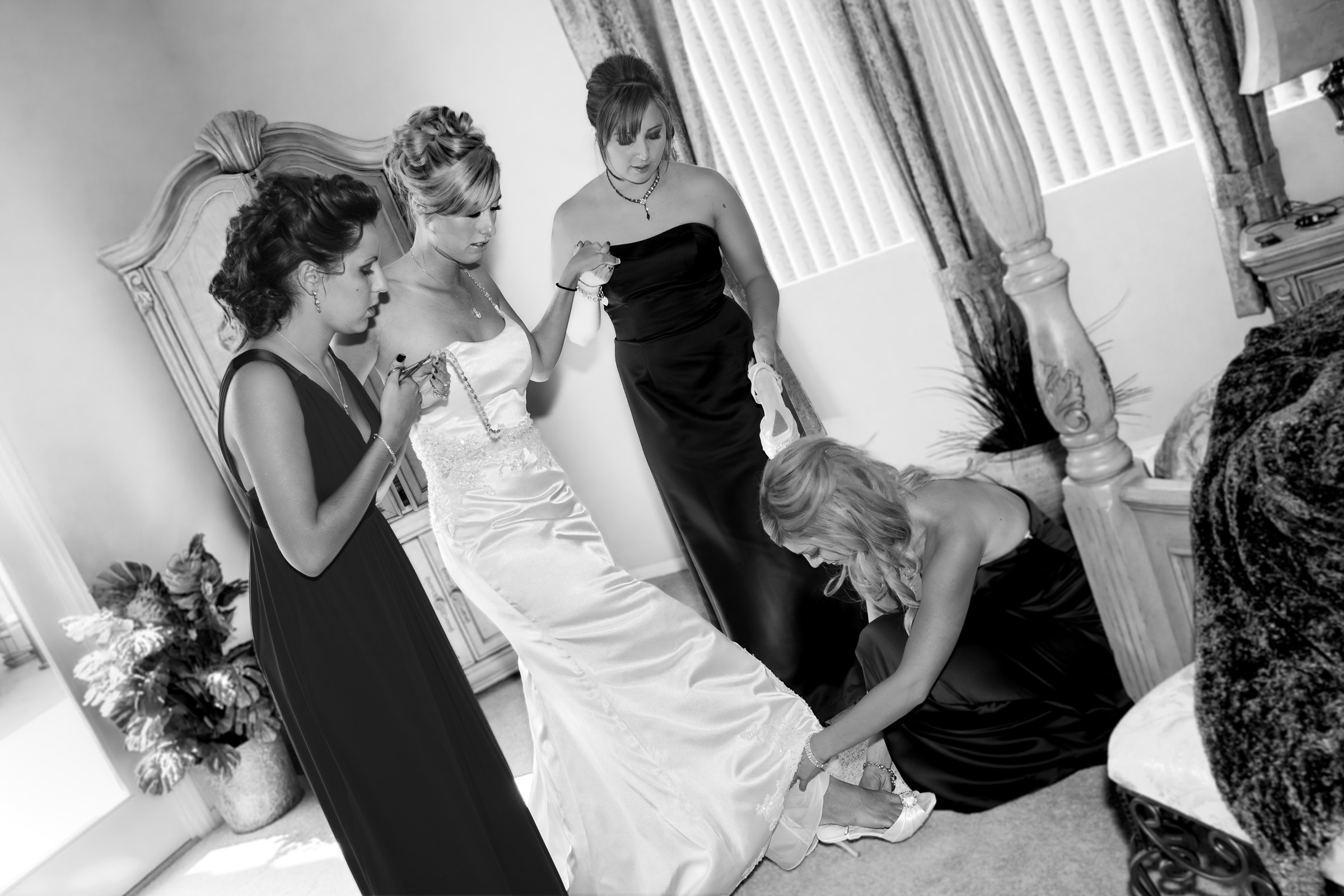 Bridesmaids assisting bride after strap broke on wedding dress while getting dressed for the wedding.